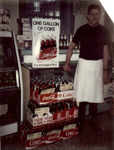 Dick Winking in Winking's Market in 1971 with his mustache.  Notice the price of $.69 for 8-Pack of 16 oz bottles of Coca-Cola.